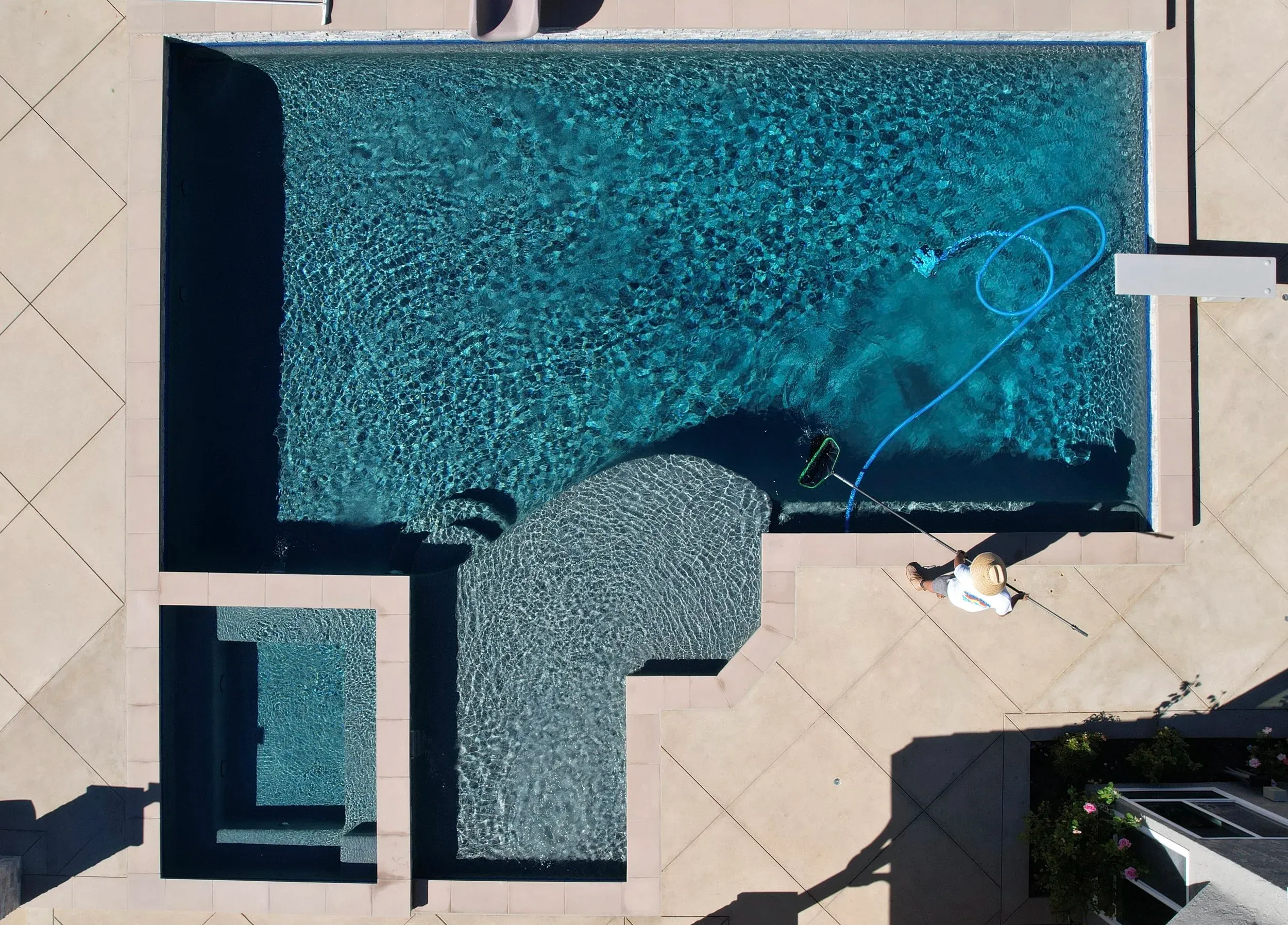 Aerial view of a pool technician cleaning a backyard pool