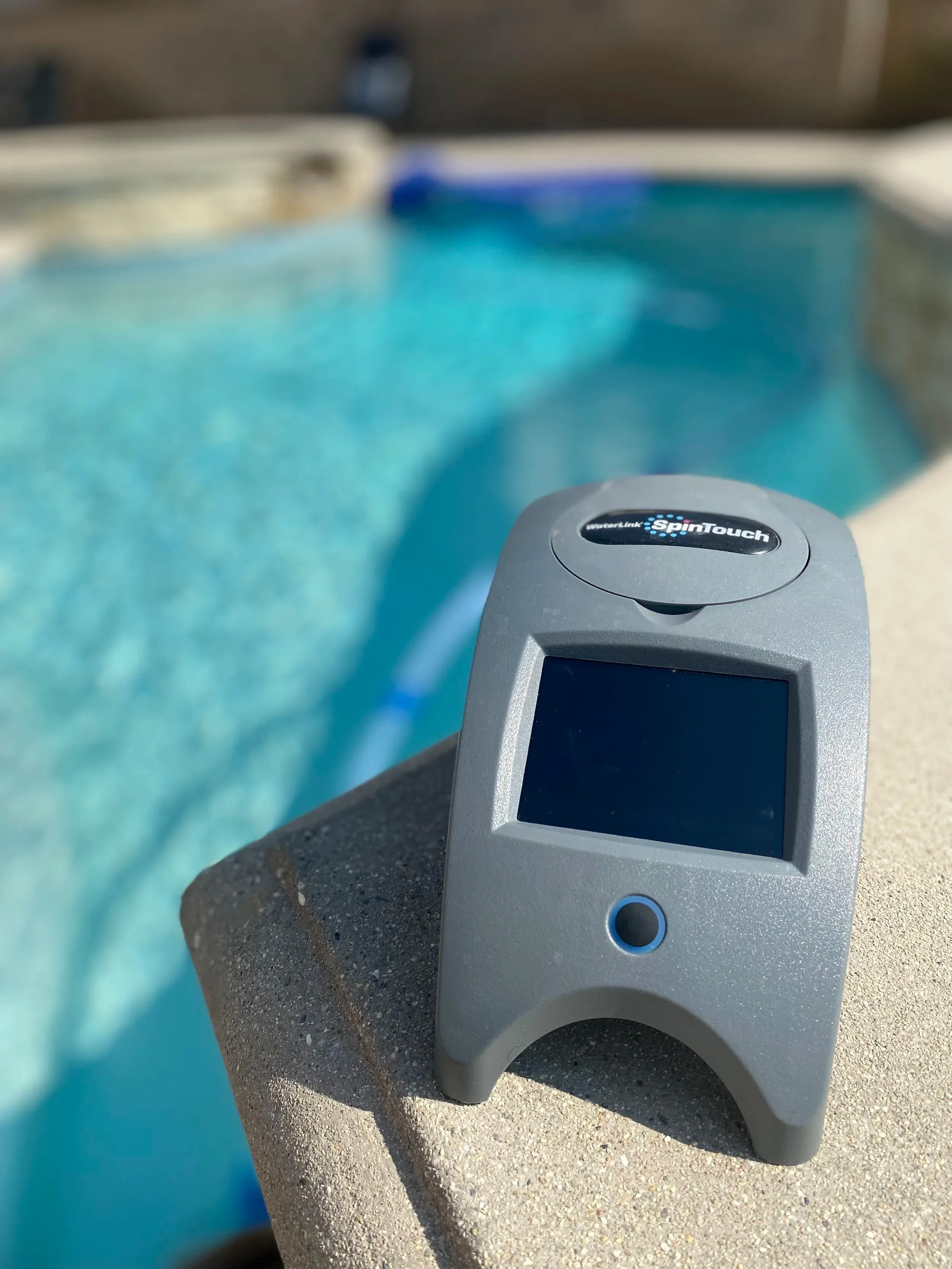 Digital water testing device sitting on the edge of a pool